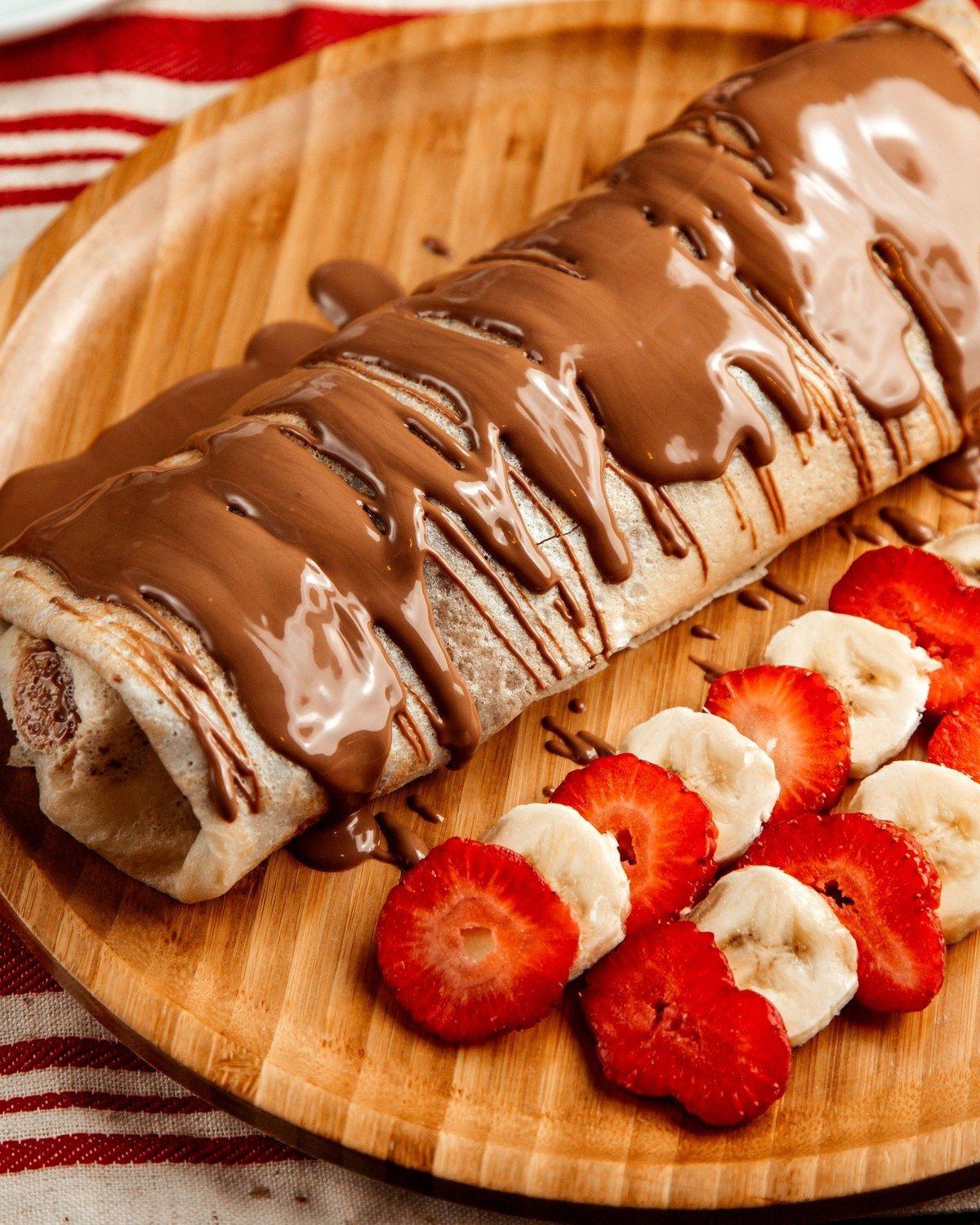 Une crêpe roulée nappée de chocolat, avec des rondelles de fraise et de banane
