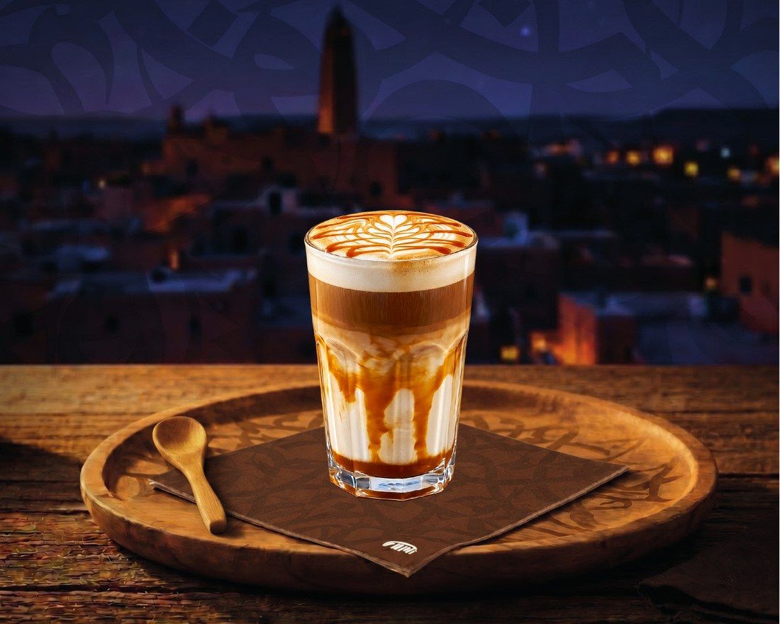 Un latte au caramel en verre, sur une serviette FAMI et un plateau en bois