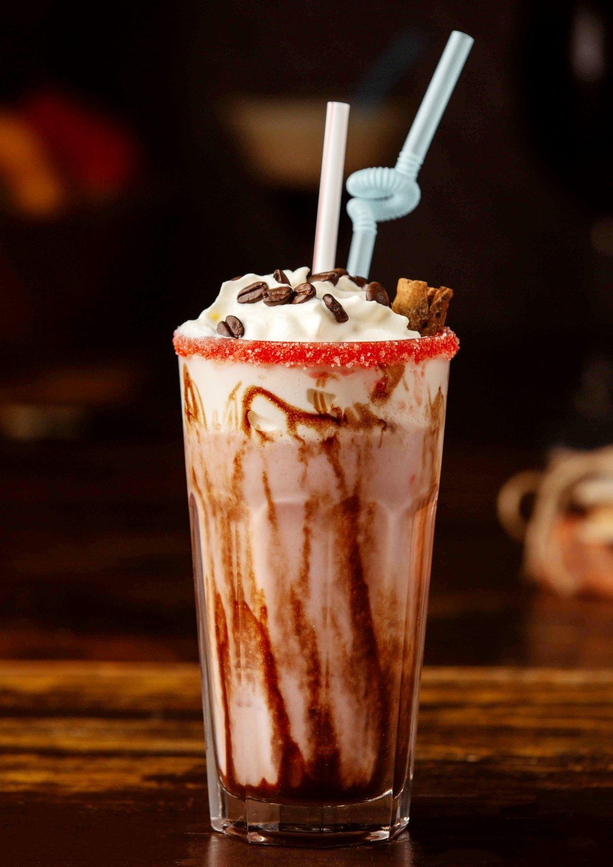 Un milkshake nappé de chocolat, surmonté de chantilly et de grains de café, le bord du verre givré de sucre rouge