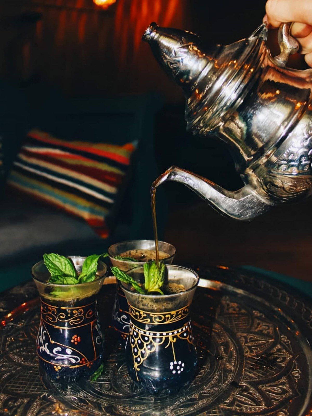 Du thé à la menthe versé d'une théière en argent dans des verres décorés