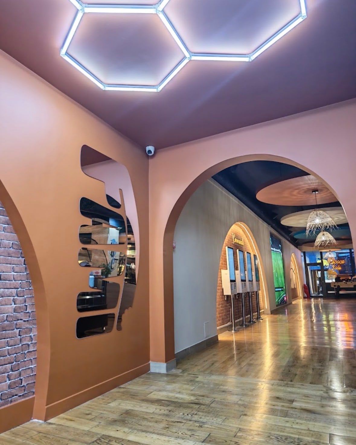 L'allée du FAMI Café : arches orange, plafond de néons hexagonaux, bornes de commande et, au fond, l'espace enfants